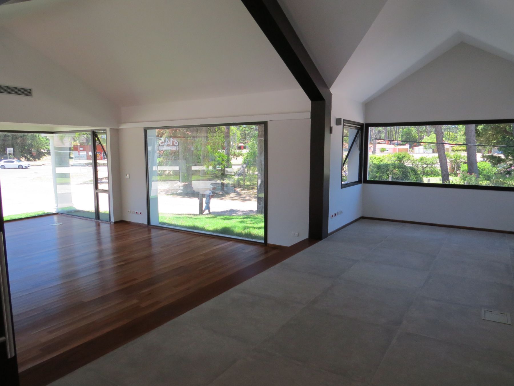 En la foto se ve la sala principal de la planta alta, con su piso de lapacho y sus techos con varias aguas. Todo rodeado de ventanales que dan hacia la calle.